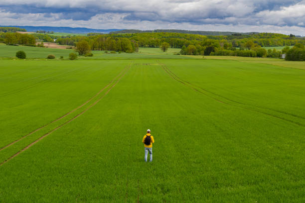 istock Aeirial view young caucasian man from back with backpack walking on spring green agriculture field. Czech landscape 1319919006