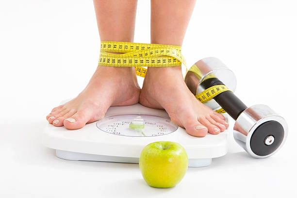 Diet Woman standing on weight scale,  legs wrapped wit tape measure, canon 1Ds mark III bound woman stock pictures, royalty-free photos & images