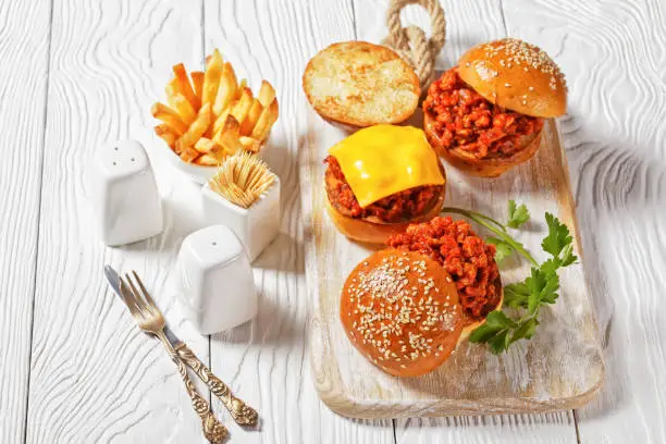 Sloppy Joe sandwiches on brioche buns served with french Fries on a white wooden board, close-up, american cuisine