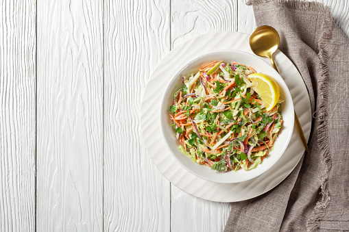 fresh summer coleslaw salad with light yogurt dressing in a white bowl on a wooden table, flat lay, free space