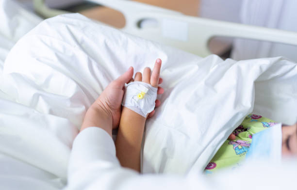 istock Young mother with protective face mask holding son's hand while lying on the hospital bed with him. Emotional Family Moment. Child vascular access 1319926206