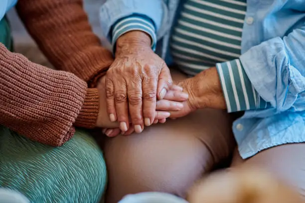 Photo of Shot of an unrecognisable woman holding hands with her elderly relative on the sofa at home