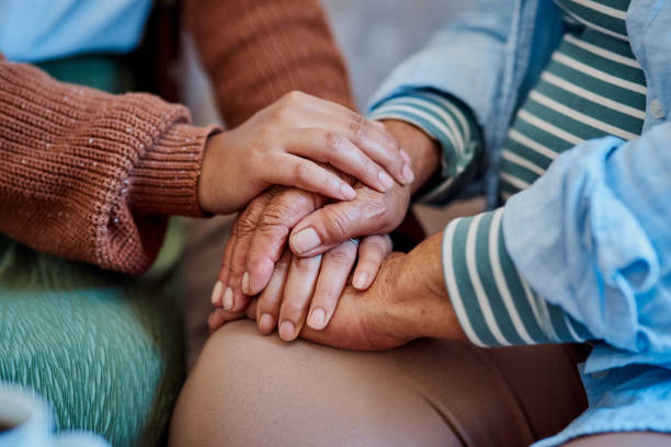 Shot of an unrecognisable woman holding hands with her elderly relative on the sofa at home stock photo