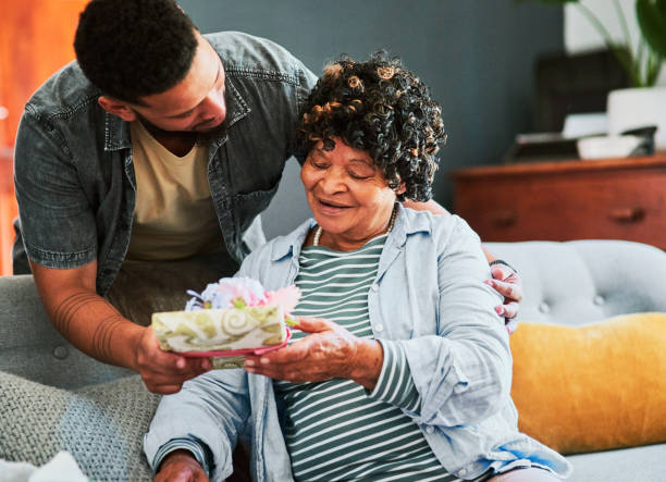 istock Shot of a young man giving his elderly relative a present on the sofa at home 1319926432