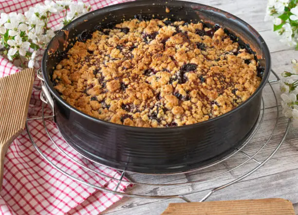 Delicious homemade and fresh baked cherry crumble cake made with sour cherries served warm in round baking pan on rustic wooden table background