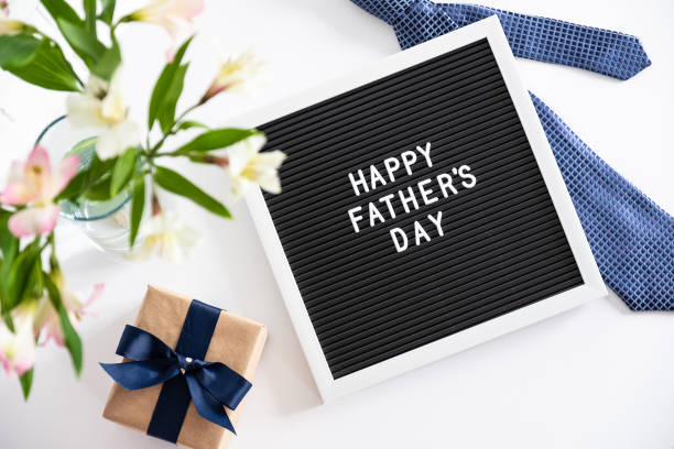 Happy Fathers Day concept. Letter board with text Happy Father's Day, necktie, gift box, boquet of flowers on table. Flat lay, top view, overhead stock photo