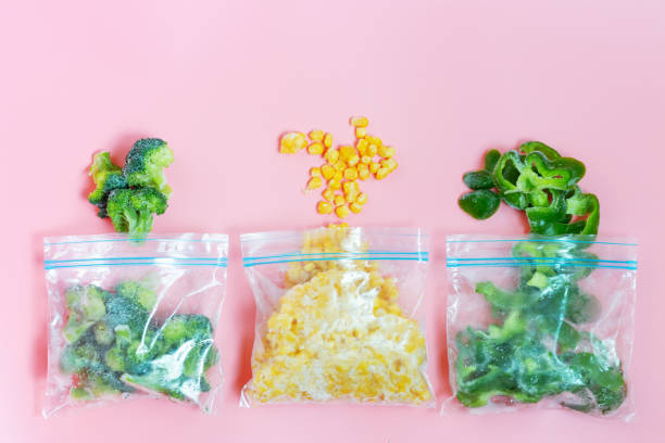istock Plastic bag and sprinkled frozen vegetables on pink background, top view. 1319930234