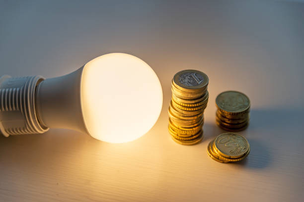 Led bulb with coins next to it. Led light bulb on, with coins beside it, on a white surface. Cost of energy, increase in energy tariffs inexpensive stock pictures, royalty-free photos & images