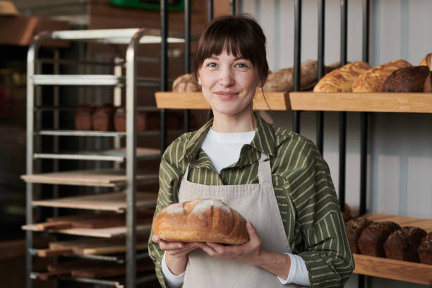 Woman with fresh bread in the shop Portrait of young woman in apron with fresh bread looking at camera in the bakery shop baker occupation stock pictures, royalty-free photos & images