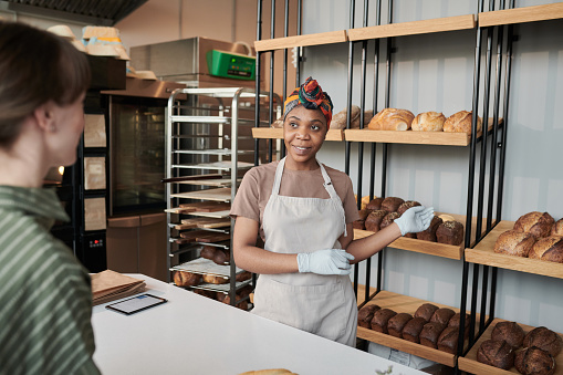 African young woman showing the fresh bread to the customer in bakery shop