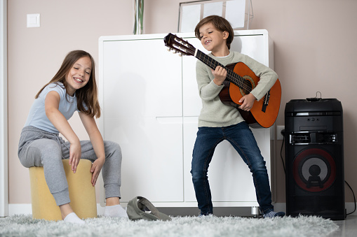 Brother and sister having fun at home. Little boy playing guitar