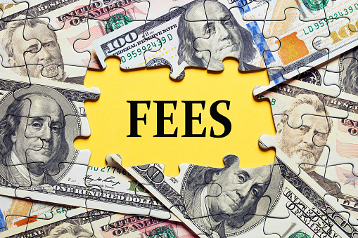 The word fees surrounded by puzzle pieces with dollar bill money. Business and finance concept for costs, charges, commissions or penalties.