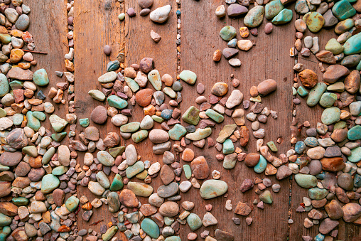 A selection of weathered colorful pebbles strewn across the old wooden floor of a beach hut at the seaside.