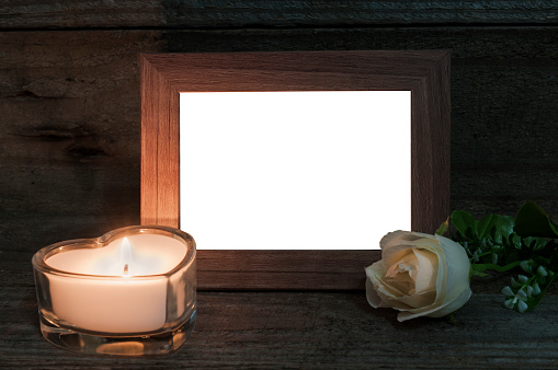 White heart shaped funeral candle and a white rose next to a blank photo frame