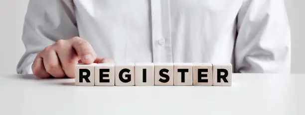 Photo of Businessman pressing his finger on the wooden cubes with the word register. registration, enrollment or subscription