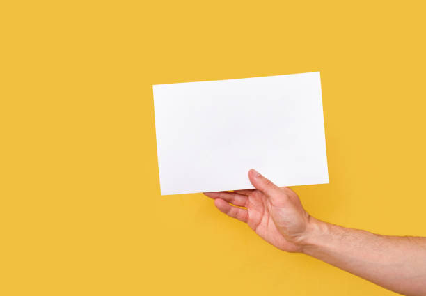 istock white paper cardboard held by one hand on a yellow background isolated on a yellow background 1319942584