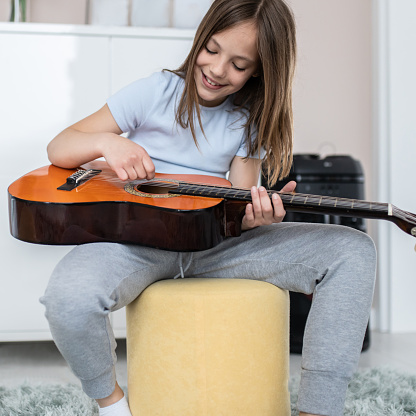 Pretty little girl practicing some new sound on a guitar at home
