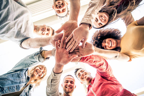 Young happy people stacking hands together outdoor - Community of multiracial international people supporting each other - Diverse culture Young happy people stacking hands together outdoor - Community of multiracial international people supporting each other - Diverse culture community college stock pictures, royalty-free photos & images