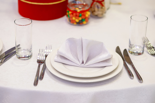 White cloth napkin on a white porcelain plate on a festive table covered with a white tablecloth