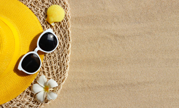 istock Yellow summer hat with sunglasses on sand. Top view 1319948709