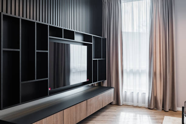 Large black shelf for large TV in a living room of an apartment. Next to a window covered with curtain.