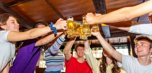 group of millennials happy friends drinking and toasting beer in irish bar restaurant.
young teenagers having fun together in vintage pub. focus on glasses. youth, joy, happy hour celebration concept - irish culture beer drinking pub imagens e fotografias de stock