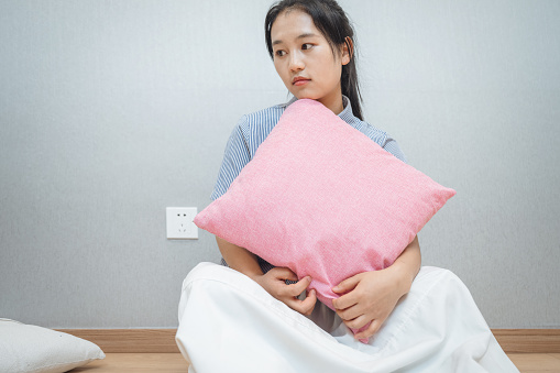 A sick girl sitting on the ground with a white cushion in a clean and tidy environment