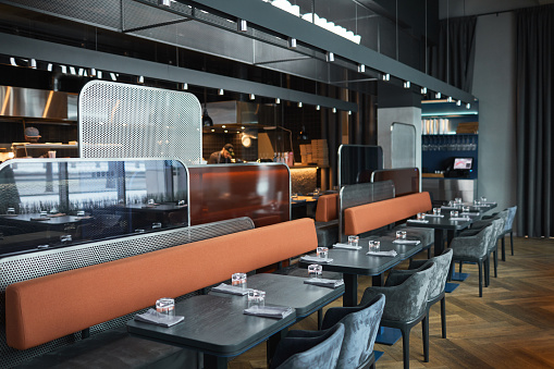 Contemporary interior of bistro cafe in black color with long sofas separated with metallic and glass panels
