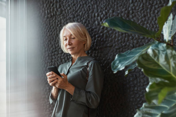 istock Mature woman with blond hair using smartphone against stone wall 1319960015