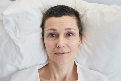 Portrait of mature woman looking at camera while lying on bed during her treatment at hospital