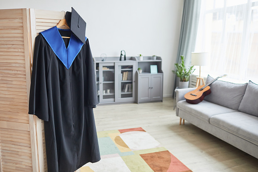 Background image of graduation gown hanging on door in cozy home interior, copy space