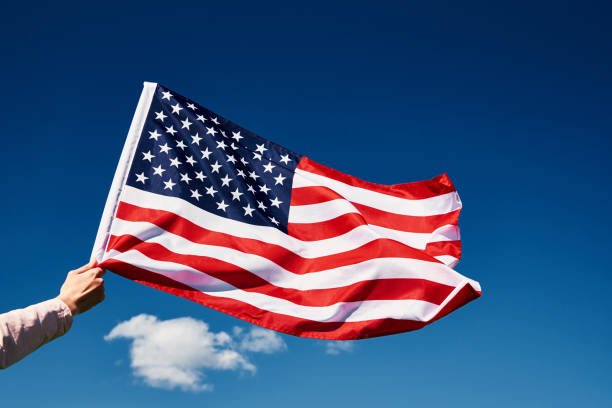 istock Waving usa flag in hand against blue sky 1319966786