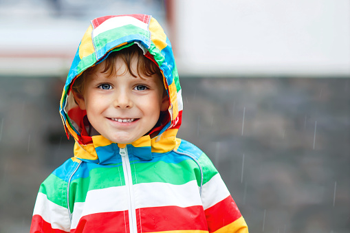 Portrait of little toddler boy playing on rainy day. Happy positive child having fun with catching rain drops. Kid with rain clothes. Children and family outdoor activity on bad weather day