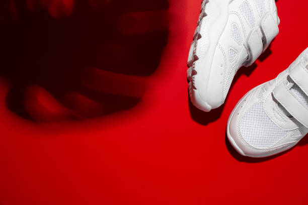 istock top view two white unisex sneakers with hard shadows from the monstera leaf isolated on a red vivid background 1319967630