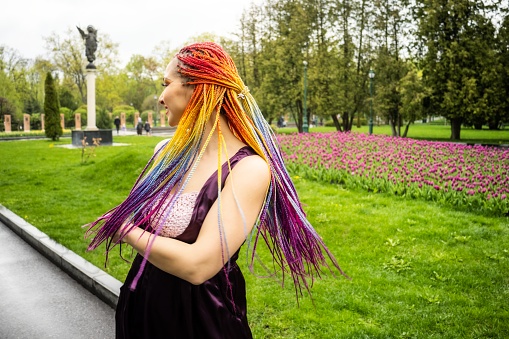 A beautiful girl with multi-colored glitter makeup and bright African braids in a purple satin dress. She smiles sweetly and rejoices at the arrival of the long-awaited spring in a blooming park.