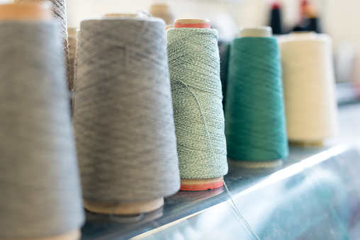 Receding row of cashmere wool on conical spools in shades of green, grey and white at a knitwear factory with focus to a reel of green yarn in the center