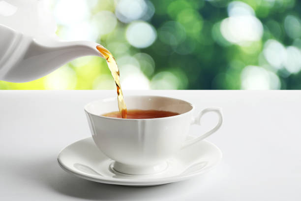 istock Pouring tea into cup on white table against blurred background 1319968923