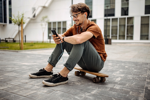 One young businessman with skateboard using smart phone outdoors