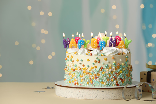 Beautiful birthday cake with burning candles and decor on white table. Space for text