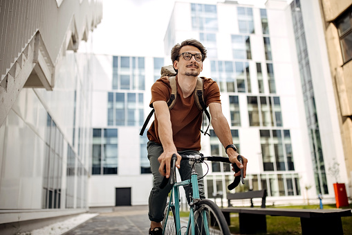 A handsome young man goes to the city with his bike. He is riding the bike, happy because of nice weather and peaceful street.