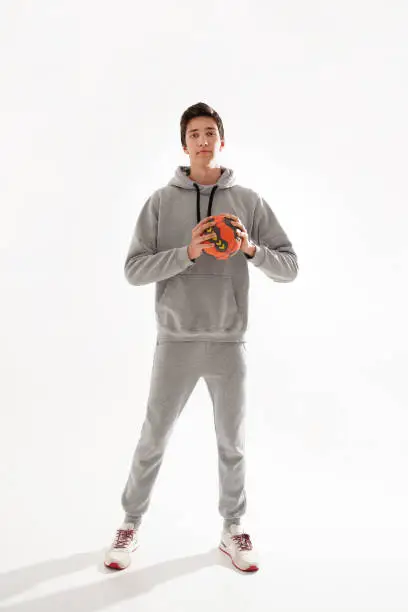 Full length photo of a young sporty boy holding handball and looking to the camera, isolated on white studio background.