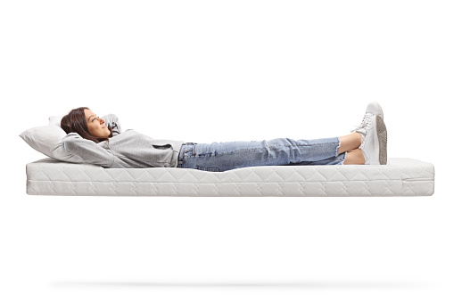 Full length shot of a young female in jeans resting on a floating mattress isolated on white background