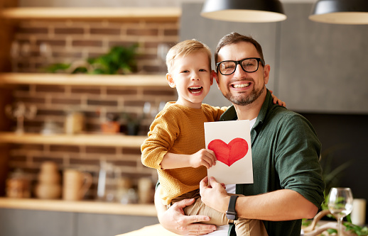 Portrait of happy family father with excited child son hugging smiling  while celebrating Fathers day together at home. Little boy congratulating giving dad homemade greeting postcard