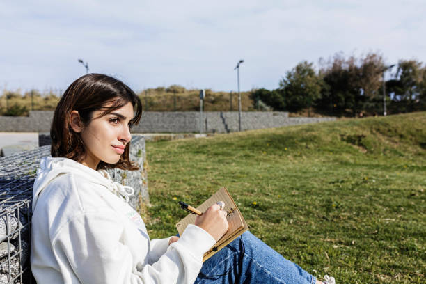 istock Young hispanic student writing in notebook while sitting in public park - Millennial woman taking notes - Education concept 1319978319