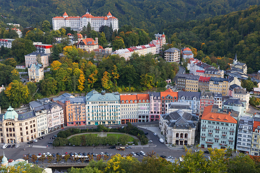 Karlovy Vary, Bohemia, Czech Republic – September 23, 2017: Top view of the autumn cityscape in a famous spa city of Karlovy Vary (Karlsbad). In the frame in the foreground is the Theatre Square surrounded by multi colored houses of the nineteenth and twentieth centuries. In the background on the left on the hill is visible the luxury Hotel Imperial surrounded by Slavkov Forest.
