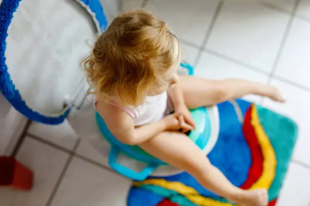 Closeup of cute little toddler baby girl child sitting on toilet wc seat. Potty training for small children. Unrecognizable face of child.