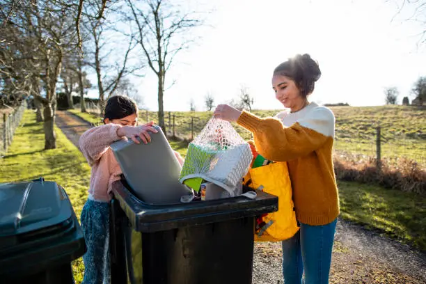 Two girls pouring their recycling waste into the bins out of bags at the bottom of their drive. They are in the North East of England.