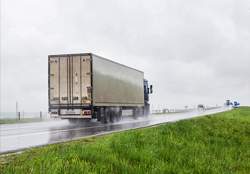 A trucker on a truck with a semitrailer transports cargo in poor visibility on the road, rain. Highway traffic in bad weather. Copy space for text, danger