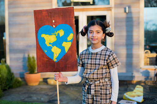 A portrait of a young girl holding a sign with  a world in the shape of a heart on it, she is fighting for climate change. She is looking at the camera and smiling while standing in the North East of England.