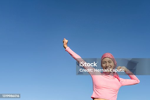 istock Young woman with cancer with gestures of victory and joy in the face of the disease. Celestial background and copy space. Hope, Struggle, Empowerment Concept. 1319986016